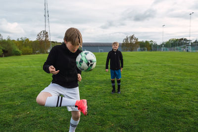 Teenage boys in sportswear playing football together on green field in summer