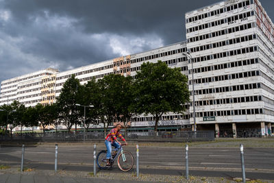 Man riding bicycle on city against cloudy sky