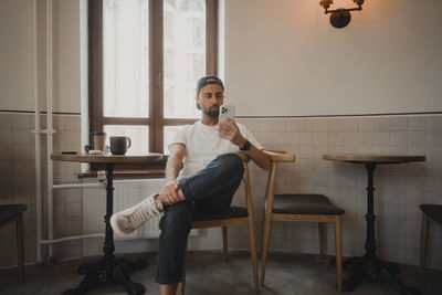 A man sits in a coffee shop and looks at the phone