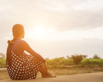 Rear view of woman sitting on land against sky