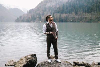 A man a groom a hipster with dreadlocks in a wedding suit stands by sea and mountains in nature