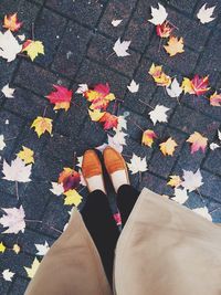 Low section of woman standing on street covered with leaves during autumn