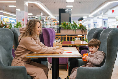 Young caucasian mother is sitting at a table in a cafe with her four-year-old son waiting