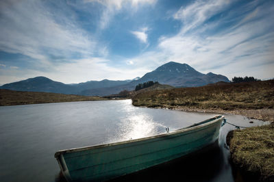 Boat moored on lake by mountains against sky