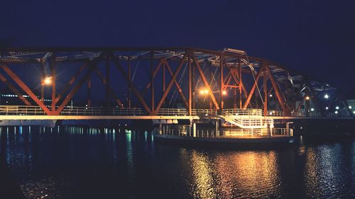 Illuminated bridge over river against sky at night