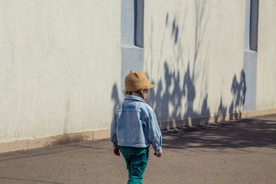 Rear view of man walking on street against wall