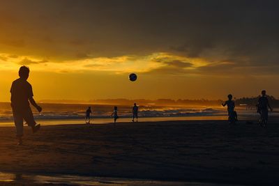 Silhouette of people playing on beach at sunset
