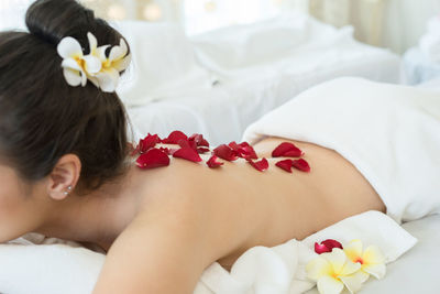 Midsection of young woman lying on massage table with flower petals on back in spa
