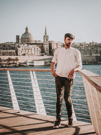 Man standing by railing over lake against sky