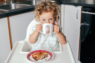  kid boy sitting in high chair eating homemade apple pie and drinking juice from cup. healthy eating 