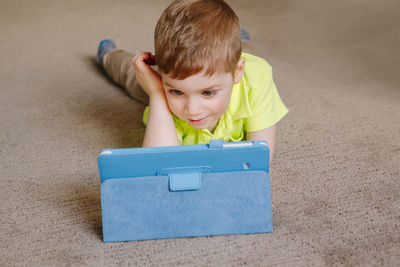 High angle view of boy using digital tablet while lying on floor