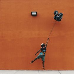 Full length of man with helium balloons flying against wall