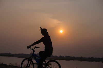 Silhouette woman riding bicycle against sky during sunset