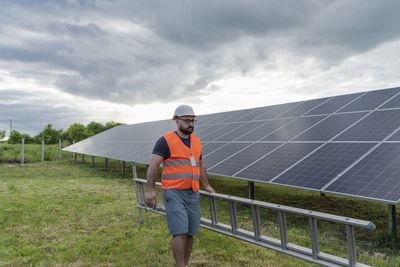 Engineer with ladder walking by solar panels