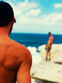 Rear view of shirtless man looking at sea against sky