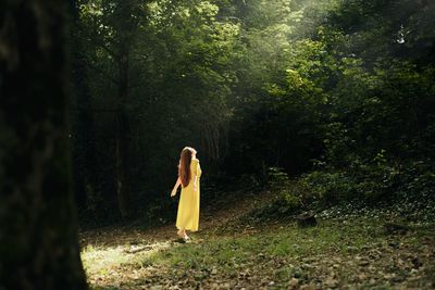 Side view of woman standing against trees in forest