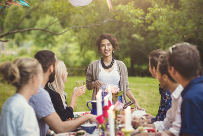 Friends listening to happy woman standing at table in garden party
