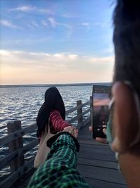 Low section of women relaxing at sea shore against sky