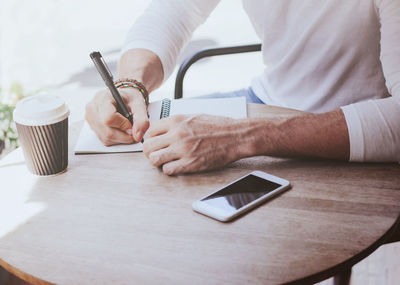 Midsection of man holding coffee cup on table