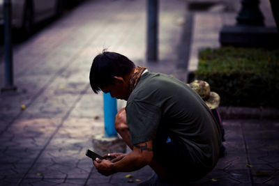 Side view of man photographing while crouching on footpath