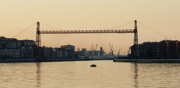 Bridge over river by buildings against clear sky