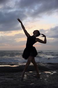 Silhouette of woman jumping in sea at sunset