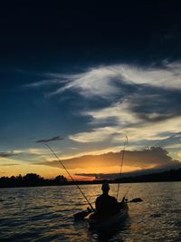 Silhouette man on boat in river against sky during sunset