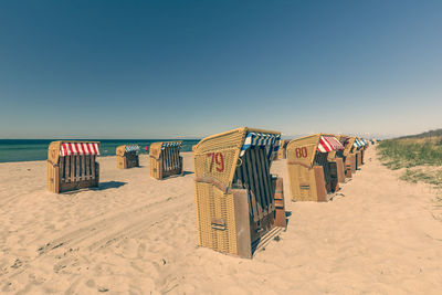 Hooded chairs on beach against clear sky