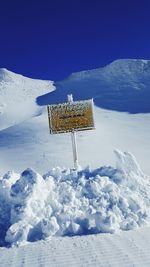 Signboard on snow covered field against clear blue sky