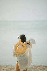 Rear view of woman holding hat standing against sea