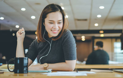 Smiling woman listening music while sitting at table