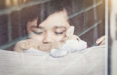 Close-up of boy with toy sleeping seen through glass window