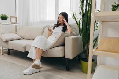 Young woman using mobile phone while sitting on sofa at home