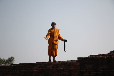 Portrait of monk standing on brick wall against clear sky