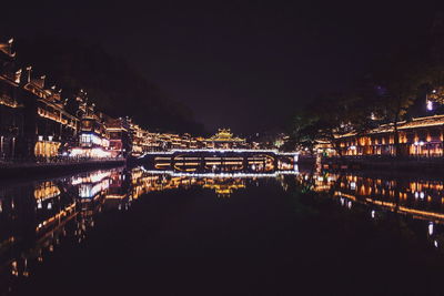 Illuminated city by river against sky at night