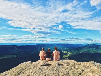 Rear view of couple sitting on mountain against sky