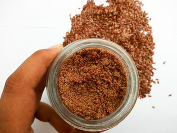 High angle view of person holding cup of ground flaxseeds against flaxseeds on  white background