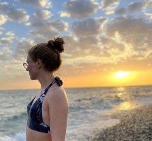 Side view of woman looking at sea against sky during sunset