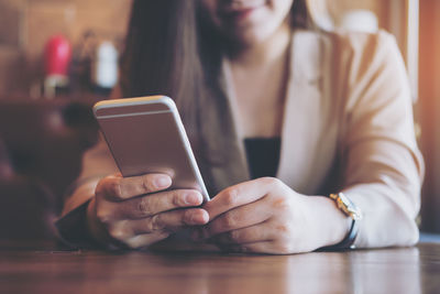 Midsection of woman using mobile phone while sitting on table