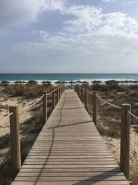 Wooden boardwalk leading towards sea against sky