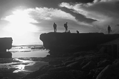 Silhouette people standing on rock by sea against sky