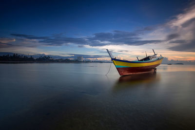 Boat moored in sea against sky during sunset