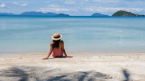 Rear view of woman standing at beach against sky