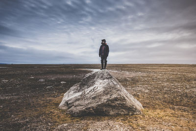 Man standing on rock against cloudy sky