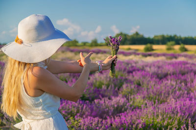 Side view of woman wearing hat holding flowers at farm