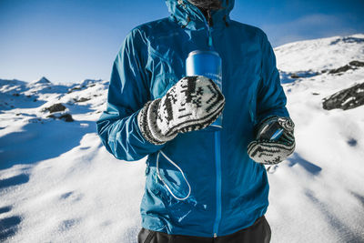 Midsection of person on snowcapped mountain against blue sky