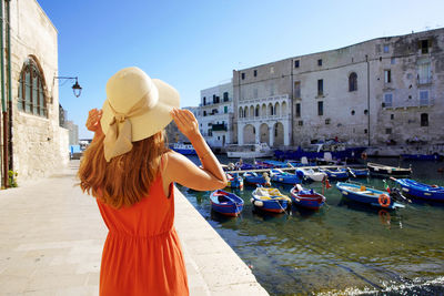 Back view of beautiful fashion girl enjoying view of monopoli ancient port in apulia, italy. 