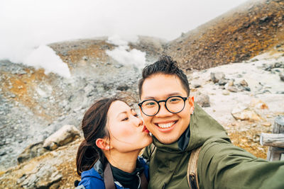 Close-up of woman kissing man taking selfie against rocks on mountain