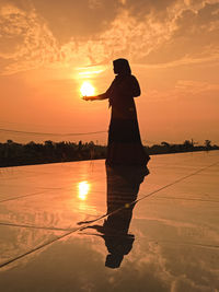 Silhouette man standing on shore against sky during sunset