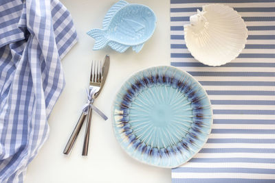 Table set in marine style empty plates in shape of fish, blue glass, fork and knife on striped 